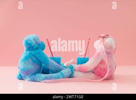 Rendez-vous romantique. Composition créative faite avec des poupées de singe roses et bleues buvant des cocktails exotiques sur fond rose pastel. Idée d'amour minimale. Banque D'Images