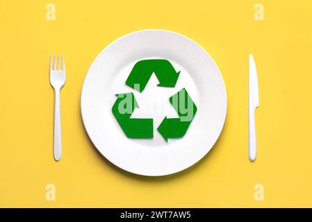 Vue de dessus du symbole de recyclage avec couverts en plastique blanc et assiette sur fond jaune. Concept de recyclage respectueux de l'environnement Banque D'Images