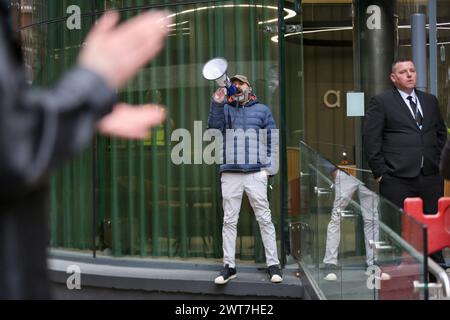 Birmingham, Royaume-Uni. 14 mars 2024. Un manifestant chante à travers un mégaphone, tandis qu'un garde de sécurité se tient debout pendant la manifestation. Les manifestants du Front de la jeunesse pour la Palestine (YFFP) et leurs partisans appellent au boycott d'AXA, affirmant qu'ils investissent plus d'un milliard de dollars dans des colonies illégales sur ce qui était autrefois des terres palestiniennes et détiennent des millions dans des investissements dans trois banques israéliennes. Ils déclarent avec ce soutien financier des sociétés comme AXA sont complices des crimes d'Israël contre les Palestiniens à Gaza et ailleurs. Crédit : SOPA images Limited/Alamy Live News Banque D'Images