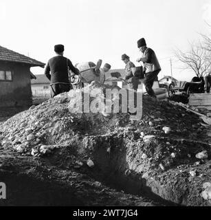 République socialiste de Roumanie, approx. 1976. Paysans fabriquant du béton à l'aide d'un malaxeur à béton et d'un tas de matériaux dans la cour d'une coopérative agricole d'État (C.A.P.). Banque D'Images