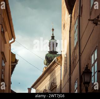 Le clocher de l'église est visible de derrière les vieilles maisons. Église de Karmelita templom dans le centre-ville de Gyor. Vieille ville hongroise sur l'après-midi ensoleillé. Banque D'Images