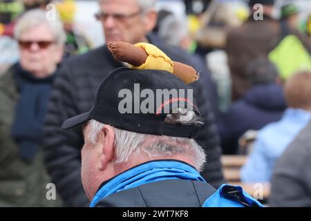 Erfurt, Allemagne. 16 mars 2024. Un homme avec une casquette de bratwurst se tient sur la place de la cathédrale à l'ouverture de la session de bratwurst avec le festival 'Rostkultur'. Un total de onze types différents de saucisses grillées peuvent être échantillonnés sur les stands. Crédit : Bodo Schackow/dpa/Alamy Live News Banque D'Images