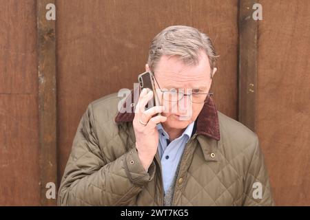 Erfurt, Allemagne. 16 mars 2024. Bodo Ramelow (Die Linke), ministre-président de Thuringe, parle au téléphone du festival 'Rostkultur' sur la place de la cathédrale lors de l'ouverture de la session de bratwurst. Au total, onze types différents de Rostbratwurst peuvent être échantillonnés sur les stands. Crédit : Bodo Schackow/dpa/Alamy Live News Banque D'Images