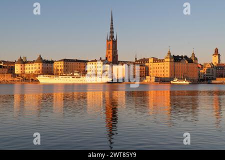 Riddarholmen église reflet dans le lac au coucher du soleil. Stockholm, Suède. Ciel bleu, fin de l'hiver. Bâtiments jaunes. Banque D'Images