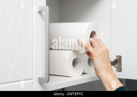 la femme au foyer sort un rouleau de papier essuie-tout de l'armoire de cuisine. essuie-tout dans le placard. à l'aide d'une serviette en papier. Photo de haute qualité Banque D'Images