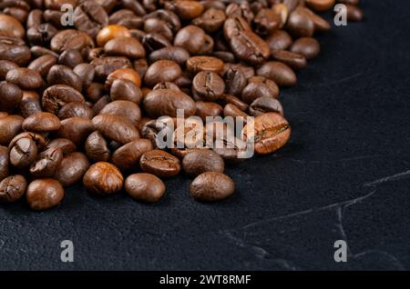 Grains de café torréfiés dispersés par une grande casserole sur un fond sombre Banque D'Images