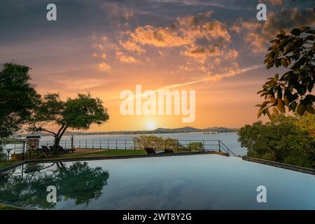 Au crépuscule, la piscine à débordement tranquille du Kandalama Heritage Hotel au Sri Lanka dispose de chaises longues à l'ombre des arbres sous un ciel bleu clair. Banque D'Images