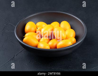 Bol en céramique noir avec des fruits de kumquat frais sur fond sombre Banque D'Images