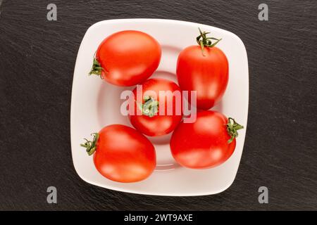 Plusieurs tomates cocktail avec plaque en céramique blanche sur pierre d'ardoise, macro, vue de dessus. Banque D'Images