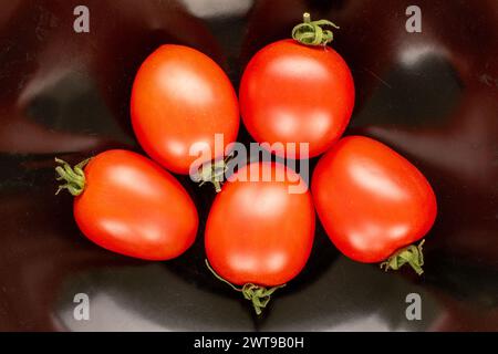 Plusieurs tomates cocktail sur une assiette en céramique noire, macro, vue de dessus. Banque D'Images