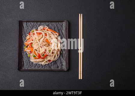 Délicieuses nouilles de riz ou udon avec du poulet, des carottes, du poivre, du sel, des épices et des herbes sur un fond de béton foncé Banque D'Images