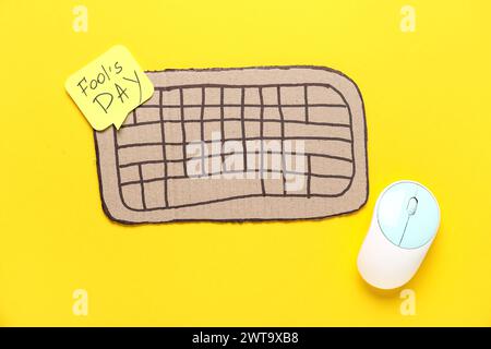 Clavier d'ordinateur de carton, note adhésive et souris sur fond jaune. Farce du jour des fous d'avril Banque D'Images