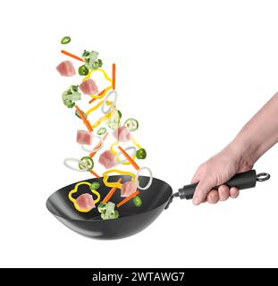 Homme jetant des ingrédients dans le wok sur fond blanc, gros plan Banque D'Images