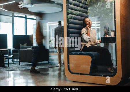Heureuse femme d'affaires assise dans un espace de coworking, parlant sur son smartphone, discutant d'un appel professionnel. Souriante et réussie, mettant en valeur sa commu Banque D'Images