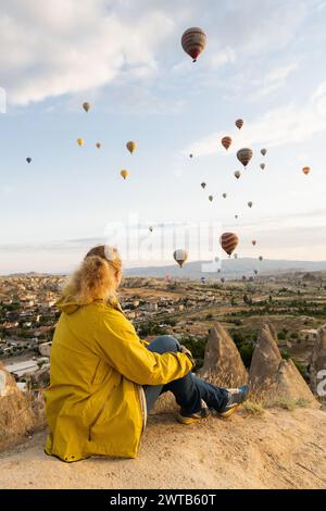 Femme blonde regardant des ballons volant au-dessus de la vallée de la cheminée de fée de Cappadoce au lever du soleil à Goreme, Turquie Banque D'Images