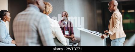 Femme d'affaires concentrée présentant à des collègues engagés lors d'une réunion d'équipe dans un environnement de bureau contemporain. L'image capture un trai d'entreprise Banque D'Images