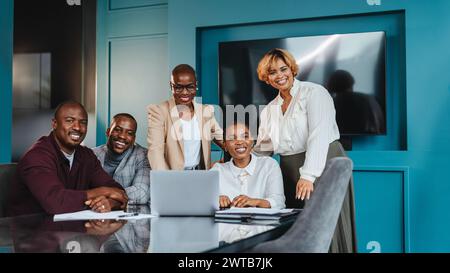 Groupe de collègues professionnels participant à une réunion d'affaires collaborative dans un bureau à thème bleu. Ils sont rassemblés autour d’un ordinateur portable, partageant des idées Banque D'Images