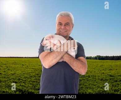 jeune cochon rose et homme devant les champs et la ferme Banque D'Images