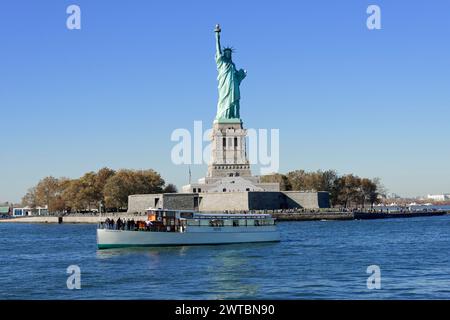 La Statue de la liberté sur une île avec un ferry devant elle sous un ciel bleu clair, Manhattan, Down Town, New York City, New York, États-Unis, Nord Banque D'Images