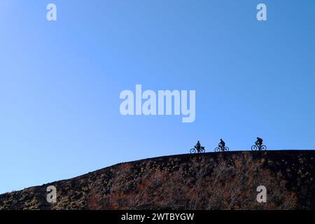 Silhouette de cyclistes sur le bord d'un cratère dans le parc de l'Etna, Sicile, Italie Banque D'Images