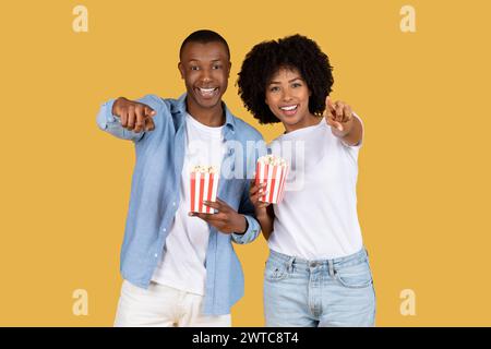 Joyeux couple afro-américain dans des vêtements décontractés tenant des boîtes de pop-corn rayées rouges et blanches Banque D'Images