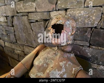 Portrait de poupée factice effrayante vintage en bois sur le fond d'un mur de pierre avec un trou sur son visage Banque D'Images