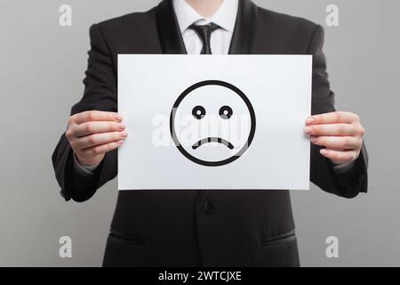 Icône d'émoticône triste de personne négative sur le papier blanc en main Banque D'Images