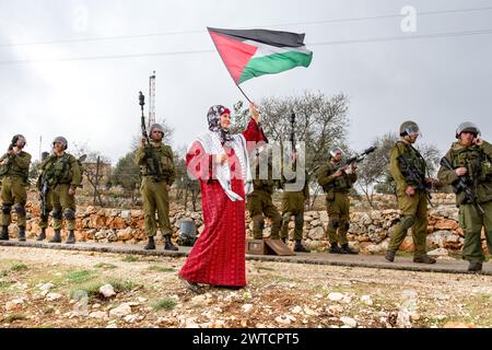 Bilin, Ramallah, Palestine. 31 décembre 2010. Un activiste palestinien marche avec le drapeau palestinien devant des soldats israéliens lors des manifestations hebdomadaires du vendredi contre l'occupation des territoriesÂ palestiniens par Israël à Bilin, Cisjordanie, Palestine, le 31 décembre 2010. Bilin, un petit village près de Ramallah, organise des manifestations hebdomadaires car une grande partie des terres des agriculteurs locaux a été annexée par les autorités israéliennes pour construire une nouvelle colonie juive. (Crédit image : © Dominika Zarzycka/SOPA images via ZUMA Press Wire) USAGE ÉDITORIAL SEULEMENT! Non destiné à UN USAGE commercial ! Banque D'Images