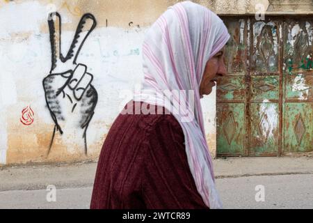 Bilin, Ramallah, Palestine. 31 décembre 2010. Une femme palestinienne marche devant un graffiti de signe victoire lors des manifestations hebdomadaires du vendredi contre l'occupation des territoriesÂ palestiniens par Israël à Bilin, Cisjordanie, Palestine, le 31 décembre 2010. Bilin, un petit village près de Ramallah, organise des manifestations hebdomadaires car une grande partie des terres des agriculteurs locaux a été annexée par les autorités israéliennes pour construire une nouvelle colonie juive. (Crédit image : © Dominika Zarzycka/SOPA images via ZUMA Press Wire) USAGE ÉDITORIAL SEULEMENT! Non destiné à UN USAGE commercial ! Banque D'Images