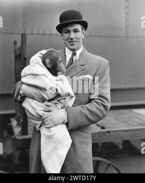 Portrait de l'acteur américain GARY COOPER en 1931 lorsqu'il est revenu à Hollywood de son voyage de chasse en Afrique avec son nouvel animal de compagnie, Toluca, un jeune chimpanzé. Photo publicitaire Paramount Pictures. Banque D'Images