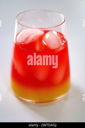 Cocktail vibrant en verre avec des glaçons, des teintes rouges, jaunes et oranges Banque D'Images