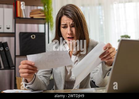 Femme d'affaires caucasienne ouvrant enveloppe lisant de mauvaises nouvelles dans la lettre se sent bouleversé assis à la table de bureau à la maison. Problèmes financiers, facture de dette bancaire pour payer, facture fiscale ou notification de faillite. Banque D'Images