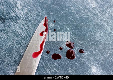 Gros couteau sanglant sur fond gris grungy avec espace de copie. Gouttes de sang sur fond rouillé. Concept de violence domestique. Banque D'Images