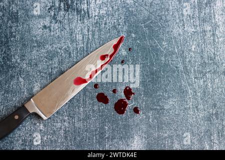 Gros couteau sanglant sur fond gris grungy avec espace de copie. Gouttes de sang sur fond rouillé. Concept de violence domestique. Banque D'Images
