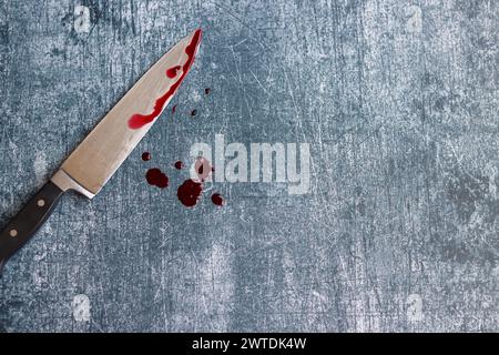 Gros couteau sanglant sur fond gris grungy avec espace de copie. Gouttes de sang sur fond rouillé. Concept de violence domestique. Banque D'Images