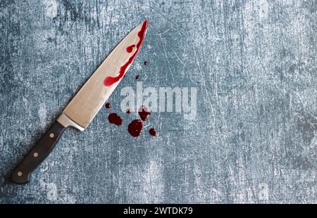 Gros couteau sanglant sur fond gris grungy avec espace de copie. Gouttes de sang sur fond rouillé. Concept de violence domestique. Banque D'Images