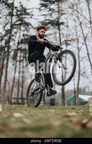 Un homme montrant de la concentration et de l'équilibre tout en faisant une cascade de roues sur son vélo de montagne au milieu de la toile de fond sereine d'un parc luxuriant. Banque D'Images