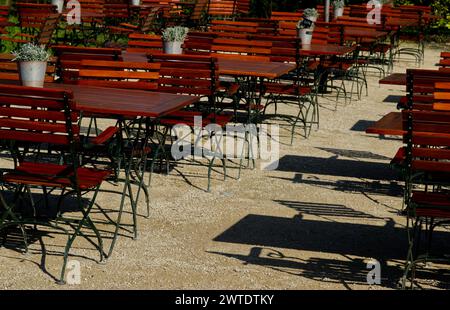 Rangées de chaises de jardin en bois brun et tables de jardin en plein soleil avec ses ombres sur le sol de sable clair à l'extérieur d'un restaurant Banque D'Images