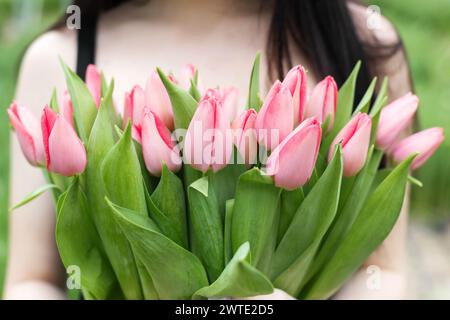 Jeune femme debout dans une grande serre et tenant des tulipes en fleurs dans ses mains. Banque D'Images