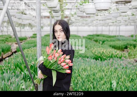 Jeune femme debout dans une grande serre et tenant des tulipes en fleurs dans ses mains. Banque D'Images