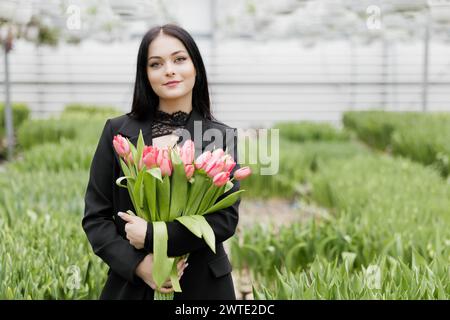 Jeune femme debout dans une grande serre et tenant des tulipes en fleurs dans ses mains. Banque D'Images