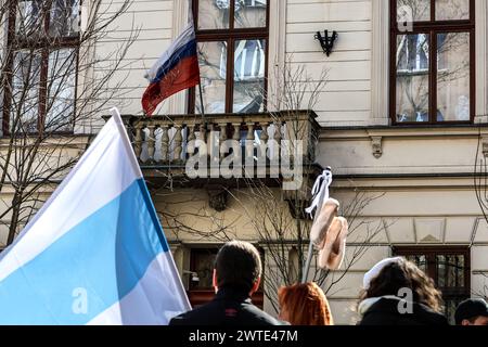 Cracovie, Pologne, 17 mars 2024. Le drapeau de la Fédération de Russie est vu sur le consulat russe à Cracovie alors qu'un manifestant tient le drapeau de l'opposition russe pendant le troisième jour de l'élection présidentielle russe à midi. Le leader de l'opposition russe, récemment décédé en prison, Alexei Navalny, puis son épouse Julia Navalna, ont appelé l'opposition à venir aux urnes le 17 mars à midi, pour montrer au président russe Vladimir Poutine le nombre de personnes qui s'opposent à son règne. Il est illégal et dangereux de protester contre le gouvernement en Russie, c'est pourquoi Navalny a suggéré l'idée de se rassembler à Banque D'Images