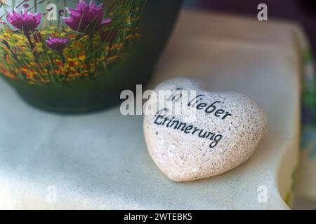 Un rocher en forme de cœur se trouve à côté d'un vase rempli de fleurs colorées, créant un arrangement doux et naturel. Il y a une inscription sur la pierre i. Banque D'Images