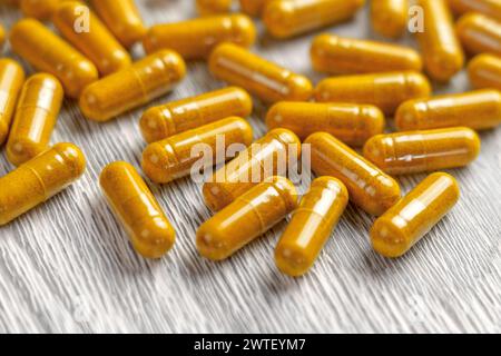 Pilules à base de plantes curcuma dans une assiette en bois. Gélules médicinales jaunes avec poudre de curcuma. Banque D'Images