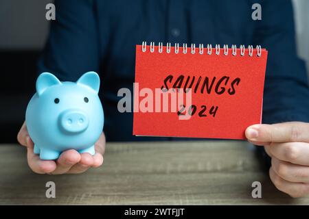 Concept Savings 2024. Accumuler de l'argent pour la nouvelle année. Budget et planification des dépenses. Un bloc-notes dans la main d'un homme d'affaires et d'une tirelire. Busin Banque D'Images