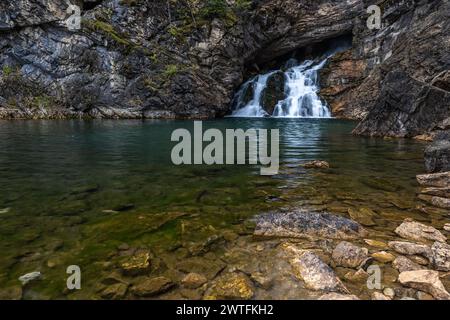 Une chute d'eau coule dans un petit bassin d'eau. L'eau est claire et calme, et les rochers autour de la piscine sont dispersés. La scène est paisible et Banque D'Images