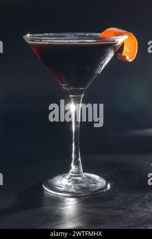 Un verre à martini avec une tranche de zeste d'orange sur le dessus. Le verre est rempli d'un liquide sombre Banque D'Images