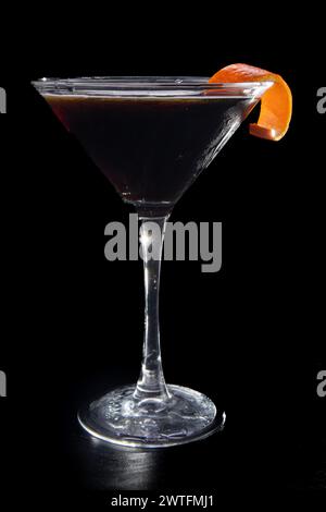 Un verre à martini avec une tranche de zeste d'orange sur le dessus. Le verre est rempli d'un liquide sombre Banque D'Images