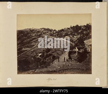 Nynee Tal. John Edward Saché, photographe (prussien ou britannique, né en Prusse, 1824 - 1882) environ 1869 deux hommes se tiennent sur un sentier non pavé devant une maison à flanc de colline. L'un des hommes tient une canne. Derrière eux se trouve la ville à flanc de colline d'Almora, avec sa vallée en terrasses et le temple Nanda Devi visible en haut à droite. Le sikhara du temple, ou dôme en forme de cloche généralement trouvé sur les temples hindous, est couronné d'une structure semblable à une galerie. (Recto, impression) en haut à gauche, à l'encre marron : '9.' ; en bas au centre, inscrit dans le négatif : '484' ; (recto, monture) en bas au centre, à l'encre marron : 'Nynee Tal. [ Banque D'Images