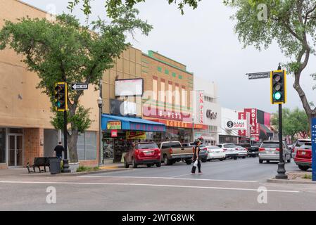 Une femme traverse la rue dans le quartier commerçant de main Street, rue bordée de magasins et de voitures garées, McAllen, Hidalgo County, Texas, USA. Banque D'Images